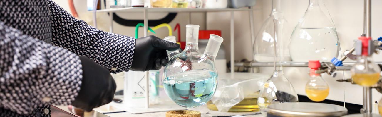 Hand holding a glass beaker with blue fluid in it